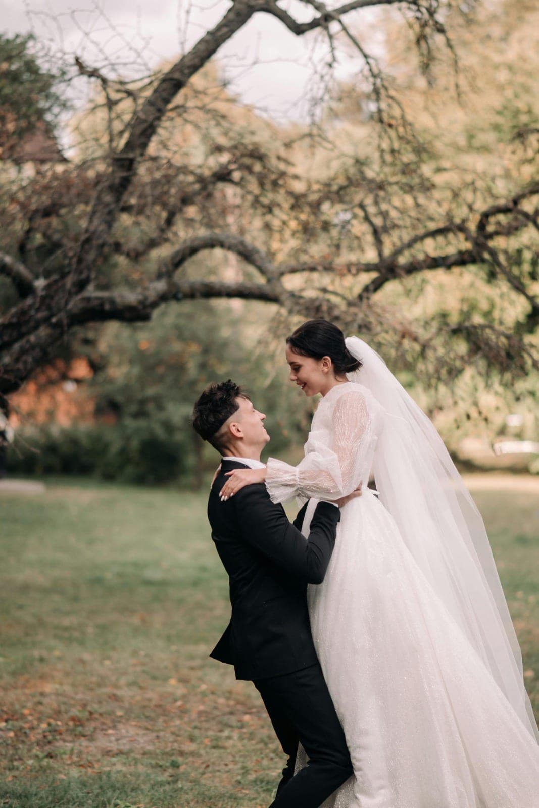 A groom lifting his bride, both laughing, beneath a tree